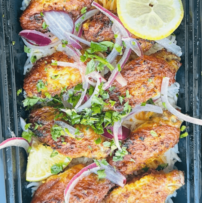 Grilled chicken wings on rice with red onions and lemon in box.